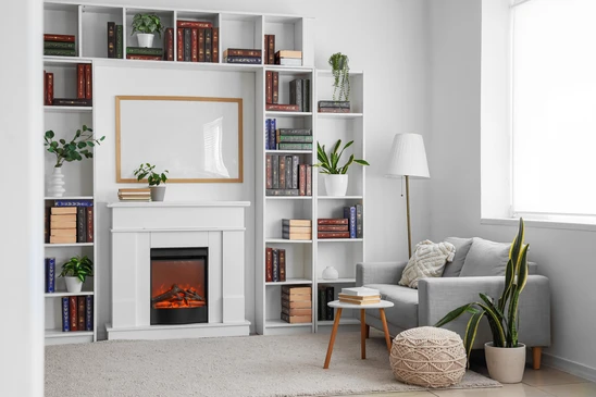 Photographie d'un salon-séjour contemporain aménagé sur mesure. Grand meuble TV ou bibliothèque laqué gris clair avec étagères intégrées en bois naturel, casiers ouverts contenant livres et objets de décoration. Base de meuble en bois clair, façades minimalistes sans poignées apparentes, éclairage LED discret intégré. Canapé gris anthracite ou taupe en arrière-plan contre mur clair. Sol en parquet gris ou carrelage grand format. Perspective permettant d'apprécier la qualité des finitions, l'intégration fonctionnelle et l'ambiance élégante et épurée de l'aménagement sur mesure.